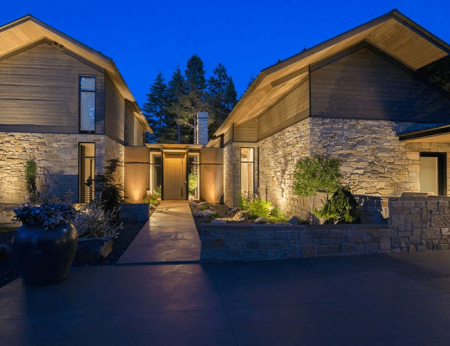 Warm architectural and landscape lighting illuminates the stone facade, courtyard entry, and planted garden beds of an Olson Kundig-designed residence in Suncadia, Cle Elum, Washington. Outdoor lighting designed and installed by Northwest Outdoor Lighting. Photography copyright © Northwest Outdoor Lighting. All rights reserved.