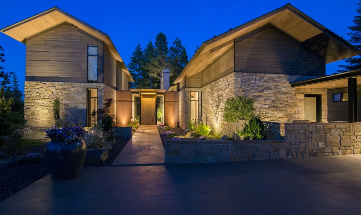 Warm architectural lighting showcases the stone-clad exterior, illuminated front entry, and landscaped courtyard of an Olson Kundig-designed Suncadia residence at dusk. Outdoor lighting designed and installed by Northwest Outdoor Lighting. Photography copyright © Northwest Outdoor Lighting. All rights reserved.