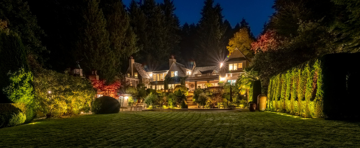 Twilight view of The Highlands Estate in Shoreline, WA with illuminated pool and landscape lighting surrounding the backyard gardens.