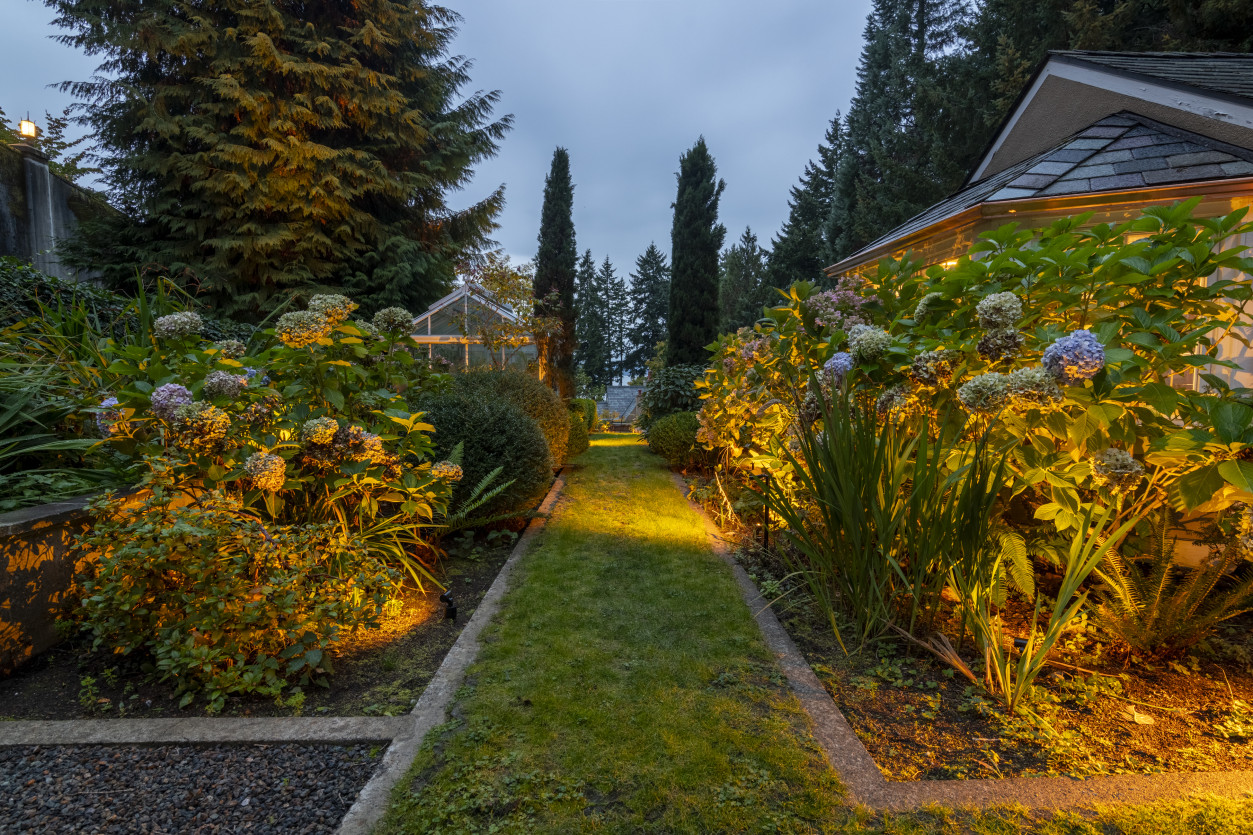 Pathway lighting through landscaped gardens guiding toward the main estate with warm architectural accent lighting.