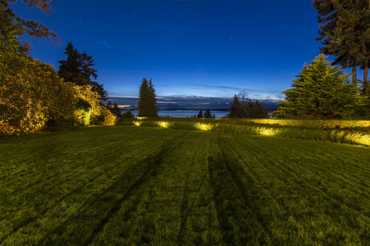 Wide landscape view with perimeter lighting across manicured lawn overlooking Puget Sound horizon at The Highlands Estate.
