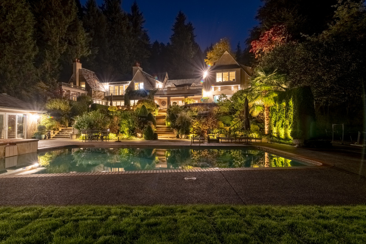 Luxury pool lighting design with full view of illuminated architecture, gardens and evergreen backdrop at The Highlands Residence.
