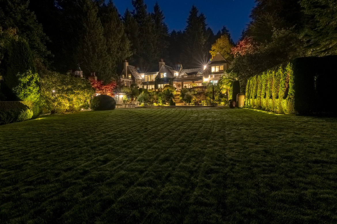 Nighttime garden and pool lighting showcasing layered hedges, formal lawn space and estate lighting beyond.