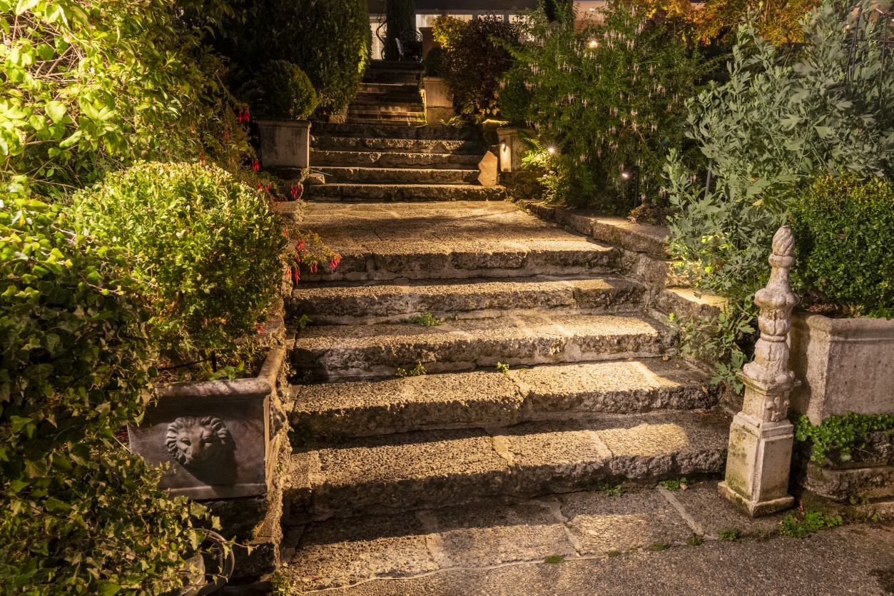 Stone stairway lighting leading down through lush gardens toward the pool area at The Highlands Estate in Shoreline, WA, illuminated with warm LED pathway lights.