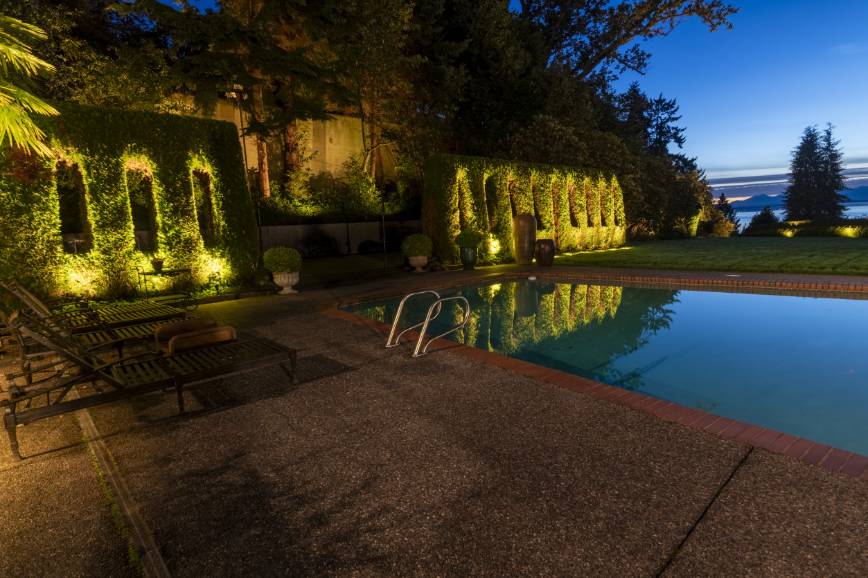 Resort-style pool lighting design with illuminated hedge backdrop and outdoor lounge seating overlooking Puget Sound at The Highlands Residence in Shoreline, Washington.