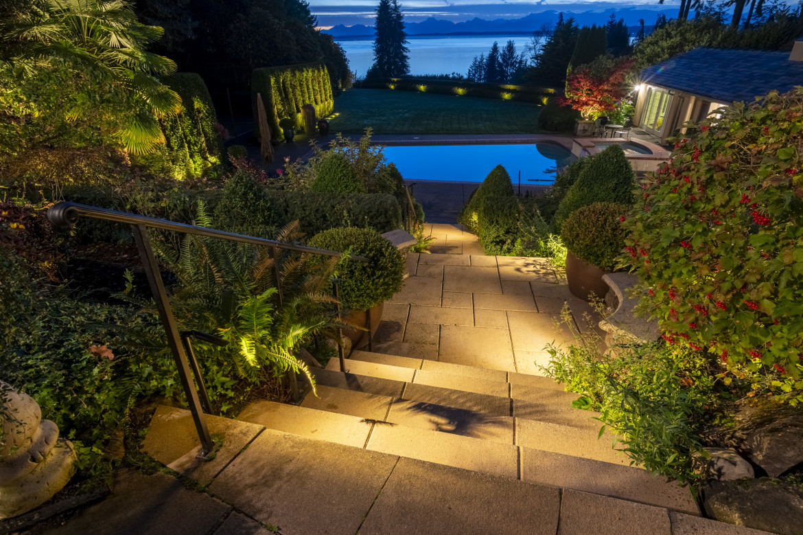 Guided pathway lighting down stone steps toward the pool deck with manicured shrubs and layered garden accents at this luxury Shoreline estate.