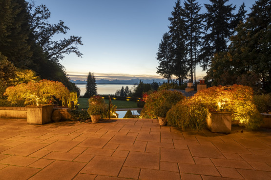 Sunset view of outdoor patio terrace and pathway lighting overlooking Puget Sound at this luxury estate in Shoreline, Washington.