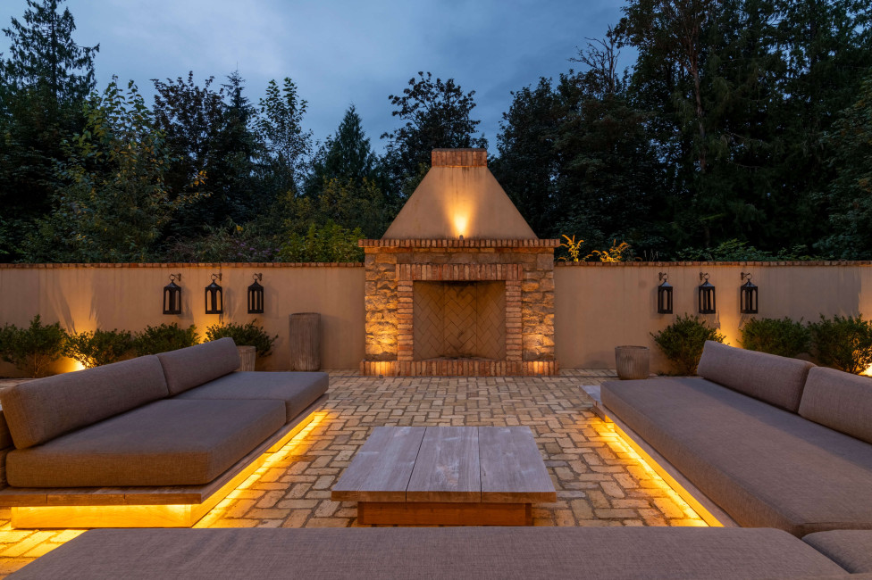 Warm integrated lighting highlights built-in outdoor seating, stone paving, and a central fireplace framed by masonry walls at Issaquah Manor in Issaquah, Washington. Outdoor lighting designed and installed by Northwest Outdoor Lighting. Photography copyright © Northwest Outdoor Lighting. All rights reserved.
