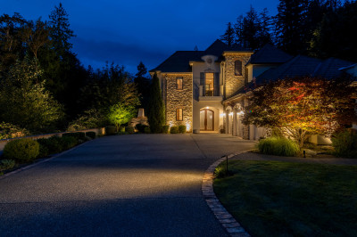 Warm exterior lighting showcases the grand front entrance, mature ornamental trees, landscaped driveway, and architectural details of Issaquah Manor in Issaquah, Washington. Outdoor lighting designed and installed by Northwest Outdoor Lighting. Photography copyright © Northwest Outdoor Lighting. All rights reserved.