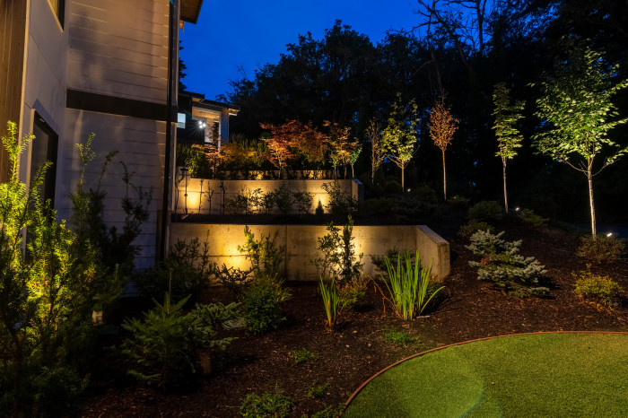 Layered garden uplighting illuminating shrubs and retaining wall landscaping near terrace steps at a Mercer Island estate.