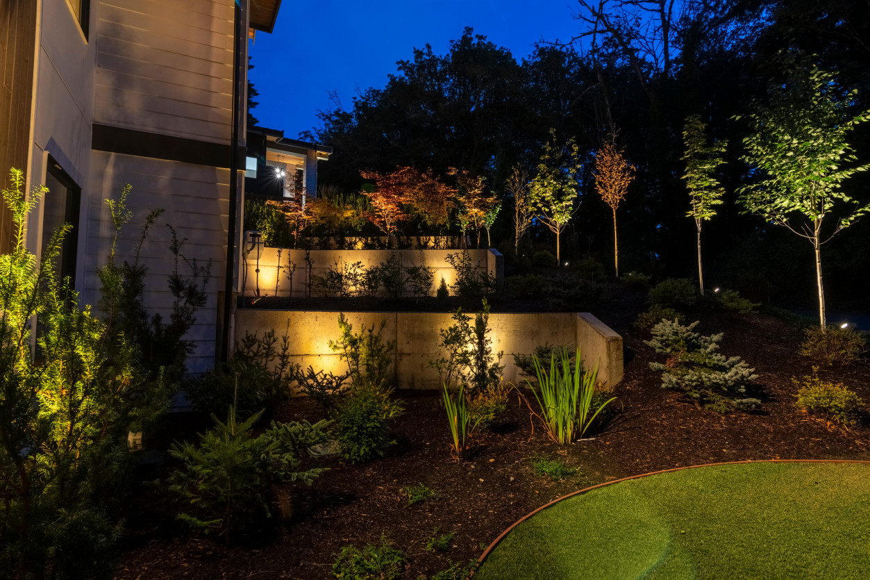 Layered garden uplighting illuminating shrubs and retaining wall landscaping near terrace steps at a Mercer Island estate.