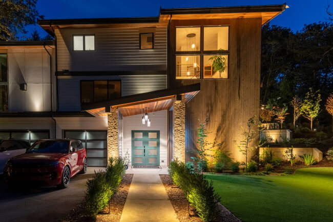 Front façade architectural and landscape lighting highlighting stone columns, wood soffits, and planting beds of a modern Mercer Island home.
