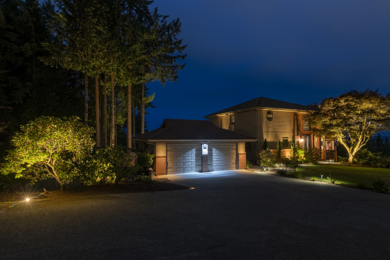 Driveway approach lighting leading to the main residence with subtle architectural illumination and surrounding cedar trees.