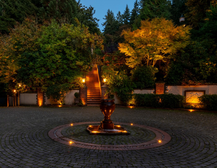 Fountain lighting detail in the circular driveway with uplighting on surrounding trees creating a dramatic nighttime arrival experience.