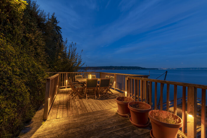 Deck seating area overlooking Puget Sound with warm Sunset Tone lighting along railing and deck edges.