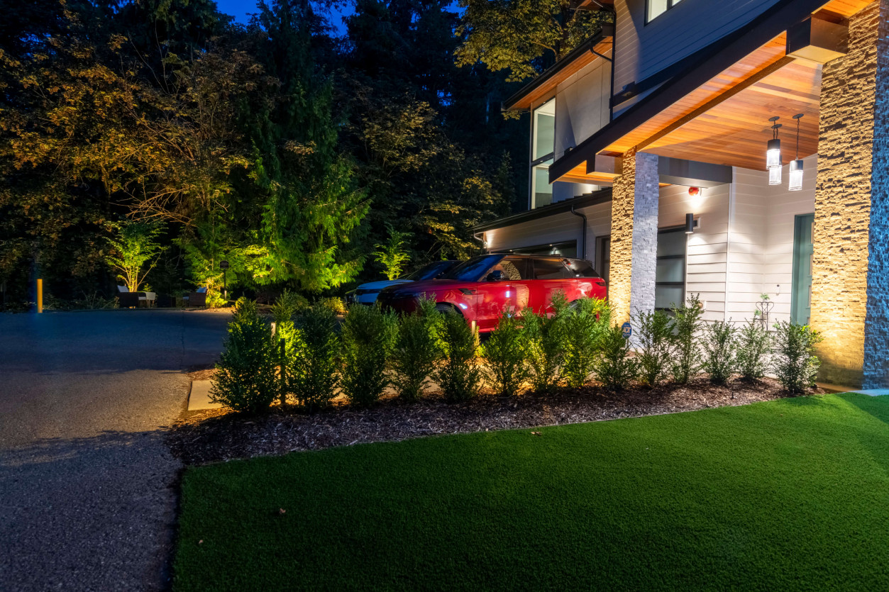 Front landscape lighting illuminating hedge row, driveway edge, and architectural elements near garage of a contemporary Mercer Island estate.