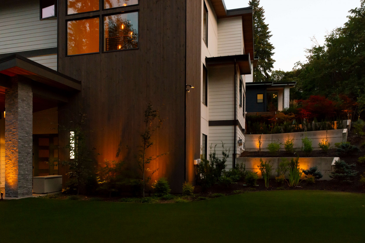 Architectural uplighting illuminating vertical wood siding and surrounding landscape plantings at a Mercer Island Contemporary Estate using Sunset Tone LED fixtures.