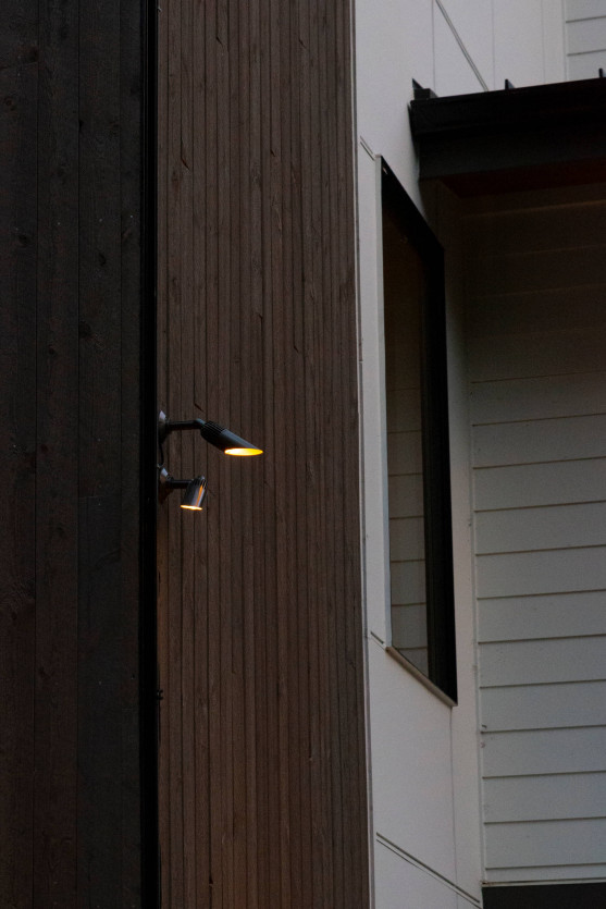 Modern wall-mounted exterior sconce providing warm illumination along wood siding at the entrance walkway of a Mercer Island contemporary home.
