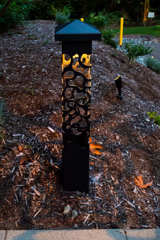 Custom decorative bollard light featuring organic cut-steel pattern, illuminating garden mulch bed and pathway edge at a Mercer Island Contemporary Estate using Sunset Tone LED lighting.