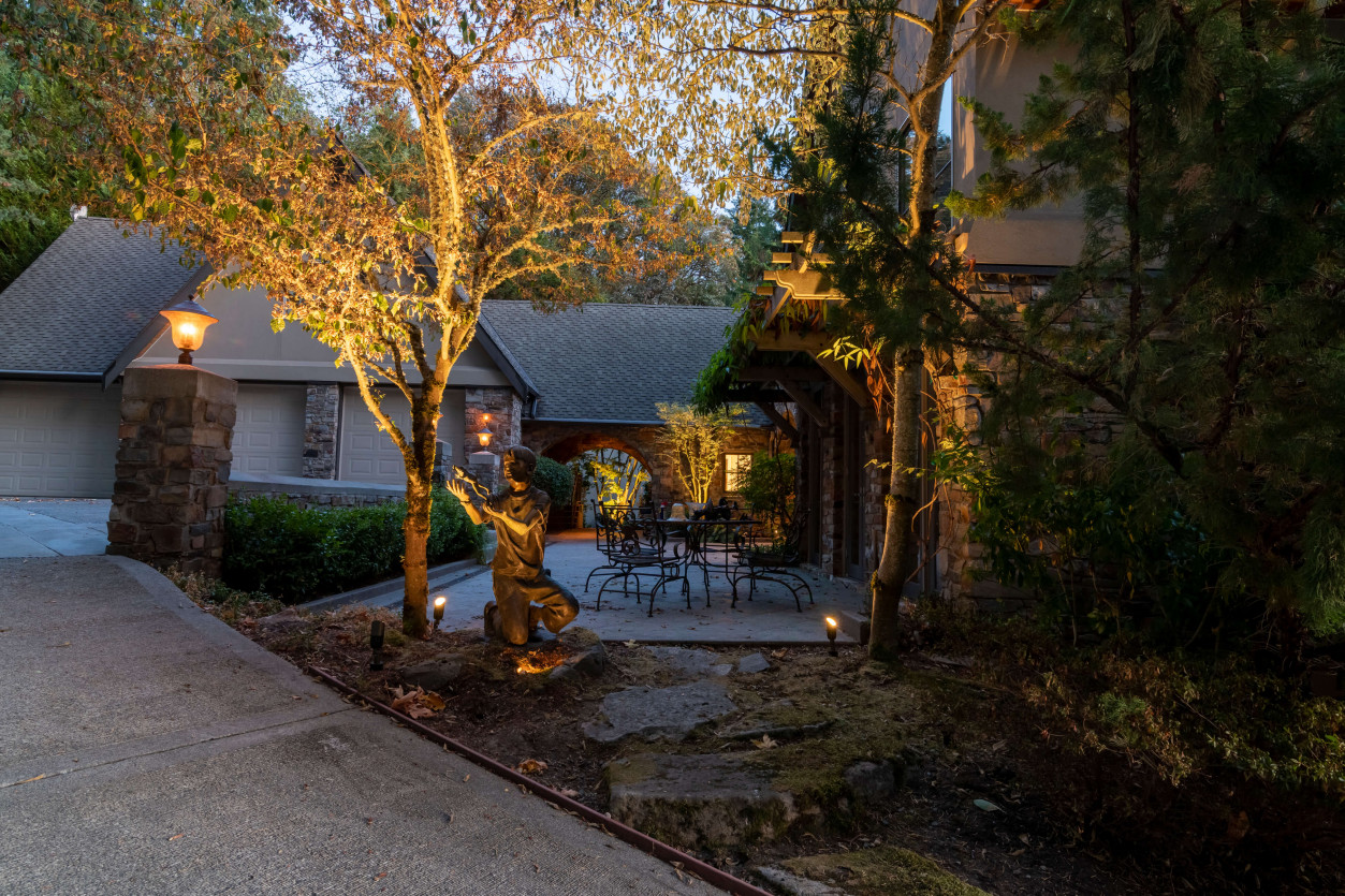 Driveway and landscape lighting guiding arrival at Sammamish estate with uplighting on mature trees and garden foliage.