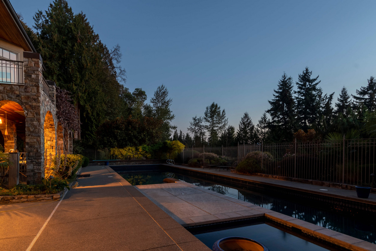 Before picture of stone patio and swimming pool edge highlighting evergreens and architectural features at a Sammamish luxury home.