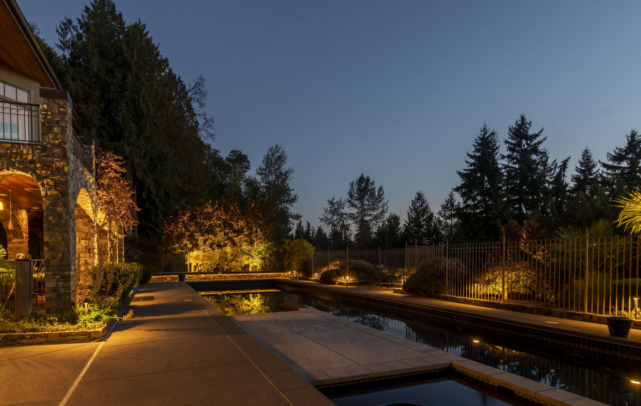 Evening pool lighting and soft landscape uplighting illuminating trees and patio hardscape at a Sammamish luxury property.