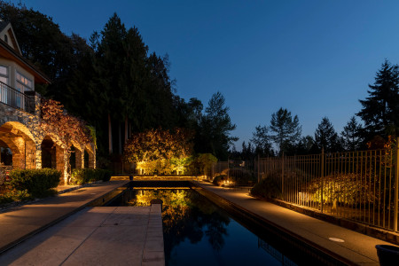 Reflections of landscape lighting on swimming pool surface highlighting stone architecture and trees at Sammamish Art & Pool Estate.