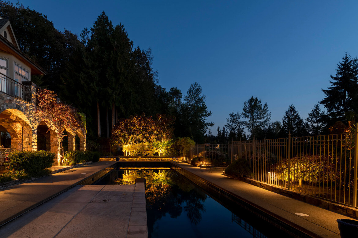 Reflections of landscape lighting on swimming pool surface highlighting stone architecture and trees at Sammamish Art & Pool Estate.