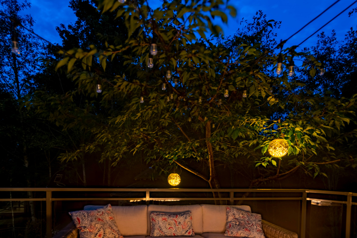 Warm deck lighting around outdoor seating and firepit area under trees at Sammamish residence.