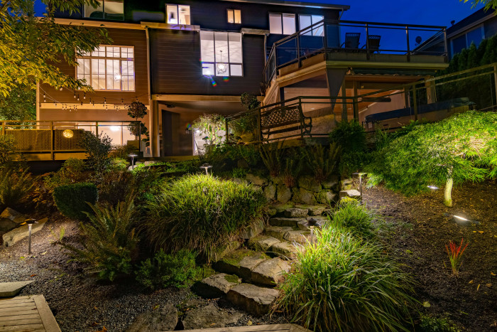 Warm down-lighting around dining deck and stairs with trees softly illuminated behind.
