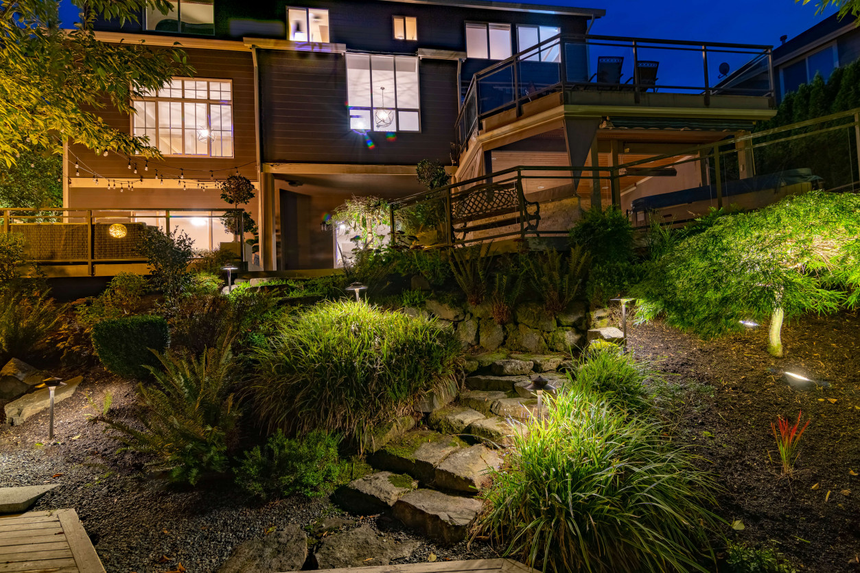 Warm down-lighting around dining deck and stairs with trees softly illuminated behind.