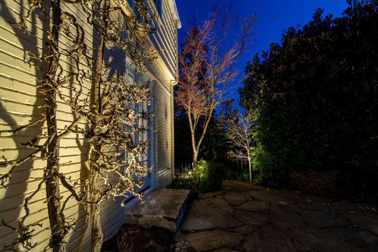 Side yard pathway lighting along garden retaining wall leading toward backyard entry.
