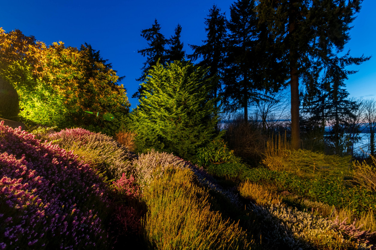 Colorful garden border and hillside lighting illuminating landscaped plantings with Sound views beyond.